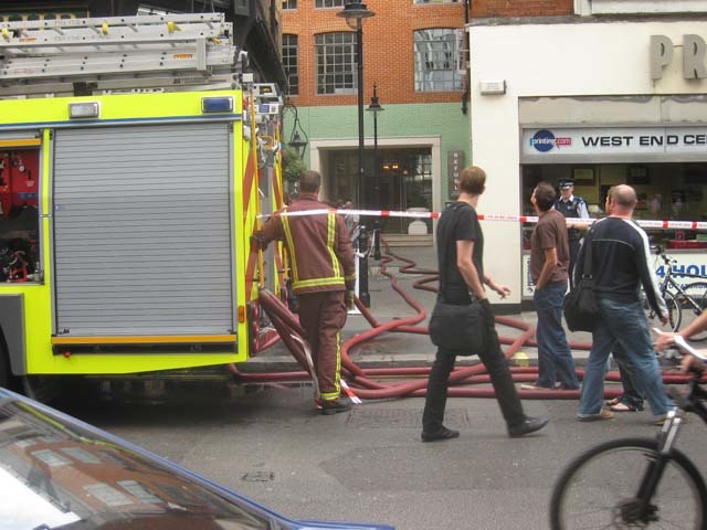 Firemen plug in hoses on Wardour Street, feeding them into the Soho Hotel's Refuel Bar.