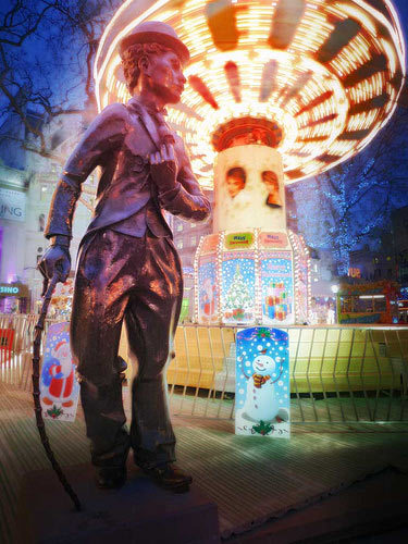 Bronze statue of Charlie Chaplin in front of Christmas funfair at Leicester Square, London 