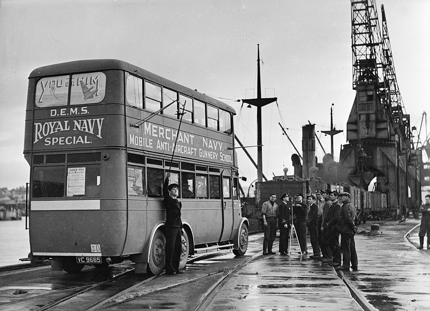 Merchant seamen receiving instruction in the art of anti-aircraft gunnery through the services of a mobile DEMS (Defensively Equipped Merchant Ships) course, from a converted bus.