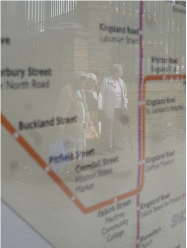 Reflection of pensioners waiting for bus, on bus map Dalston Lane, E8 by tributory