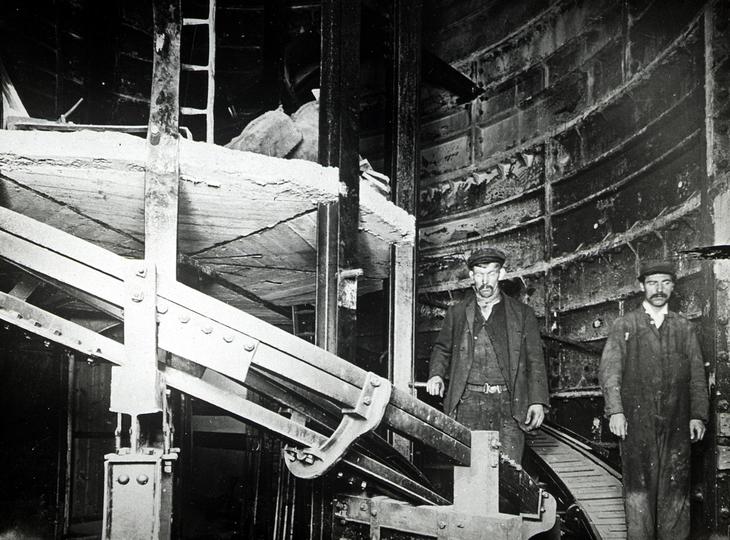 Two very glum looking workmen in flat cap stand next to the spiral staircase