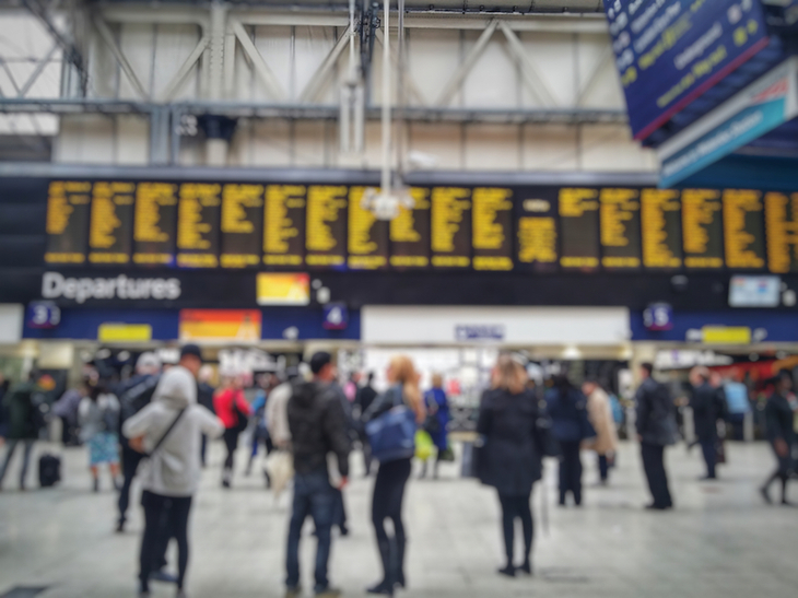 People on a train concourse looking up at blurred out platform indicators