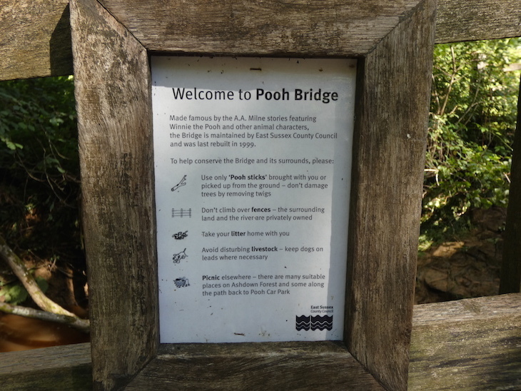 A sign in a wooden frame, welcoming visitors to Pooh Sticks Bridge