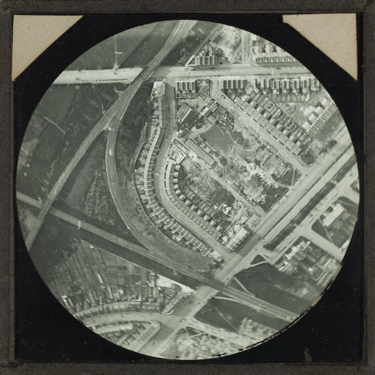 A circular view of streets of London from about 600 metres up, in black and white. Railways curve to the left of image.