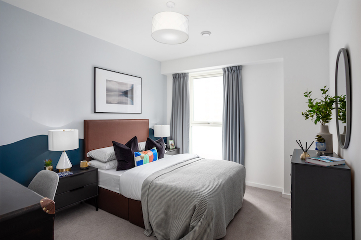 A bedroom with curtains open and modern furnishings in grey, white and blue.