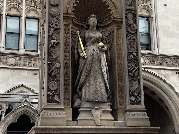 Queen Victoria statue in stone with gold-leaf orb and sceptre. She stands within an artfully carved niche, with symbols of science and progress.