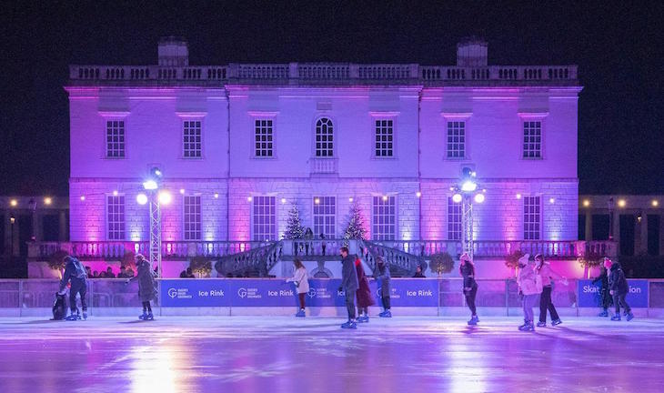 Queen's House Greenwich facade, with an ice rink in front of it at night, both illuminated purple, with skaters on the ice