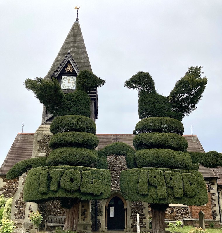 Two topiary cocks face each other in front of a church spire.