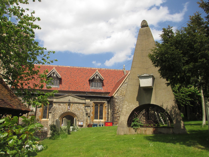 A red-roofed church with a wedge-shaped monument in the foreground.