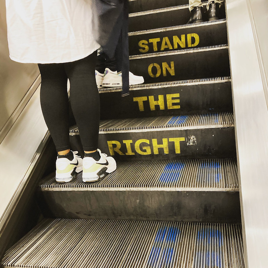Two people stand on the left of an escalator, even though the sign says stand on right.