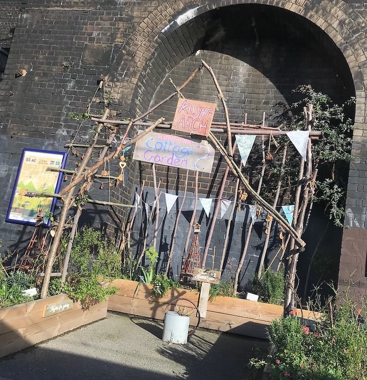 A ragged-looking pop-up garden on a railway platform, with a bamboo cane trellis