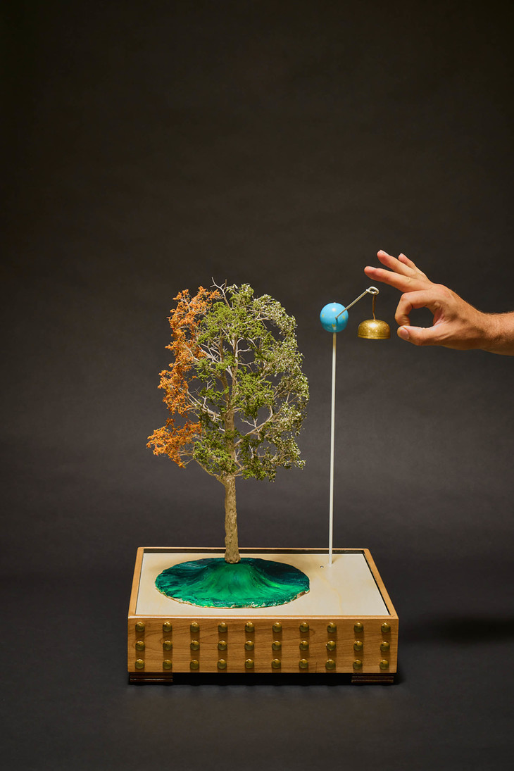 a tiny tree with a tiny bell on a pole next to it - about to be flicked by a hand