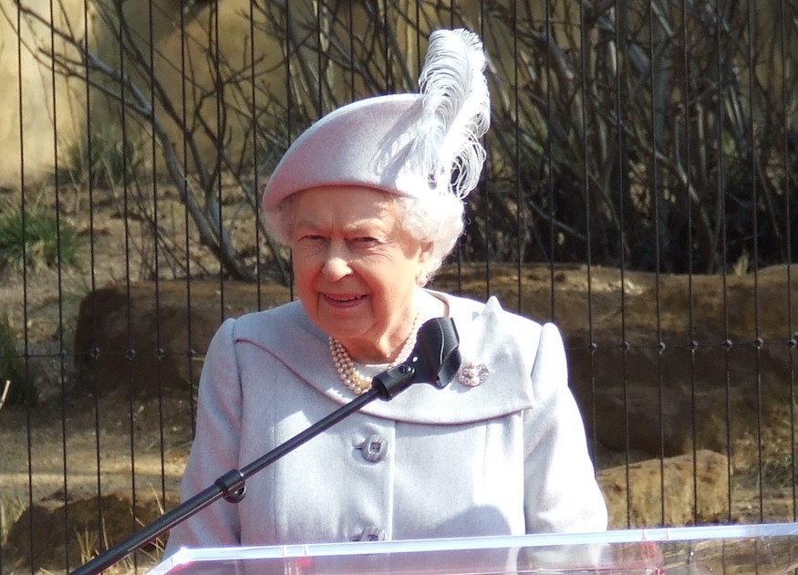 Queen Elizabeth II in front of the lion enclosure at London Zoo, wearing a light lilac jacket and hat.