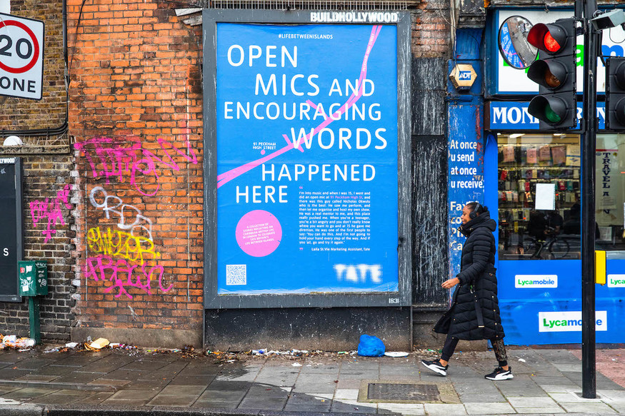 A woman walks past a billboard that says: open mics and encouraging words happened here