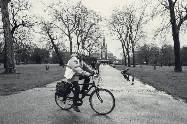 A man biking in Hyde Park, with the Albert Memorial in the distance.