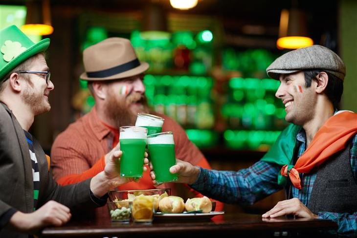 three guys in hats cheers each other with pints of green liquid