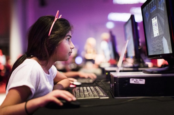 A girl uses and old-fashioned computer. The background is blurred and purple