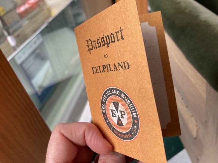 An orange 'passport' with Eel  Piland written on the front. It is clutched in a hand