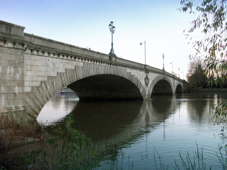 A three arch stone bridge reflects in the river