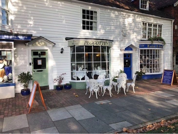 A terraced building with white weatherboarding. In the middle is a sign above a window which says 'Peggotty's', and white tables and chairs outside on the pavement