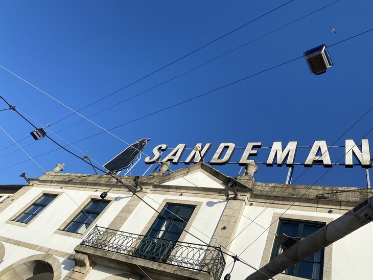 A big Sandeman sign on top of a white building with cable cars passing overhead