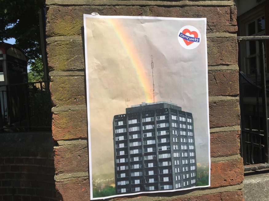 A picture stuck to a brick wall of Grenfell Tower, with a rainbow shooting out from the top