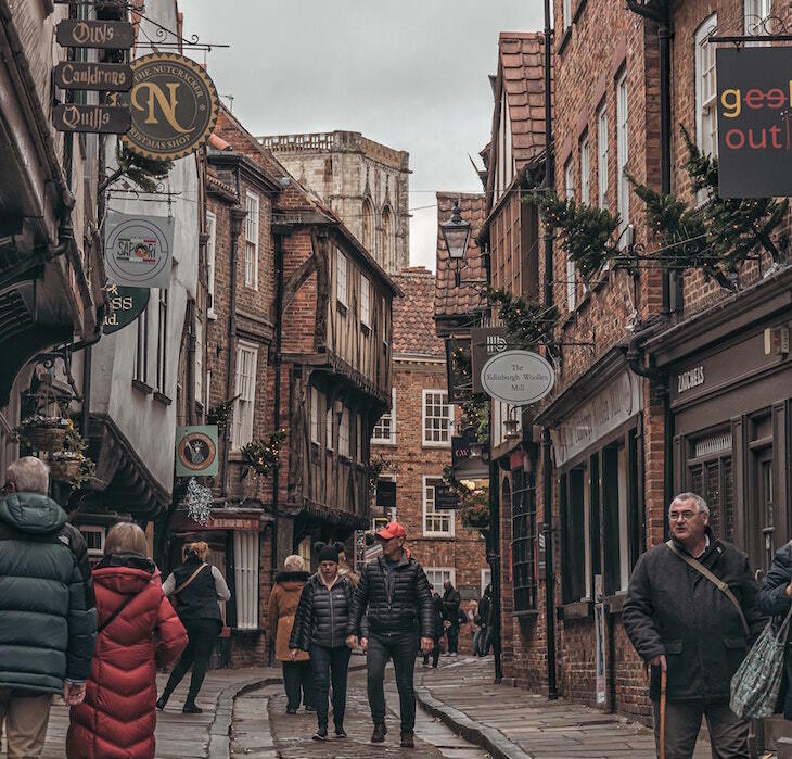 Looking down The Shambles, a narrow pedestrianised street, where the top of the opposite buildings almost touch at one end. The tower of York Minster is in the background.