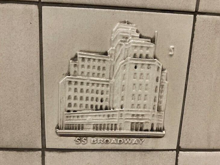 A mucky beige tile with a depiction of a large art deco office block in relief