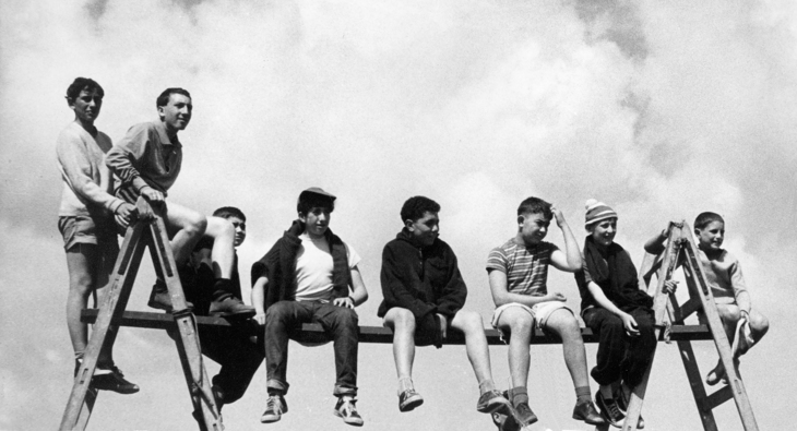 A group of boys balancing on a beam held up by two ladders