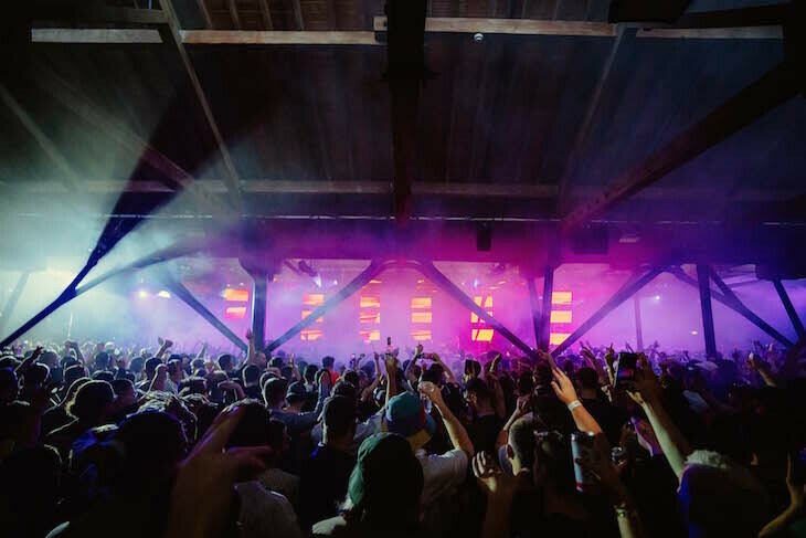 People dancing in a near-dark room at a festival, with purple lights towards the stage