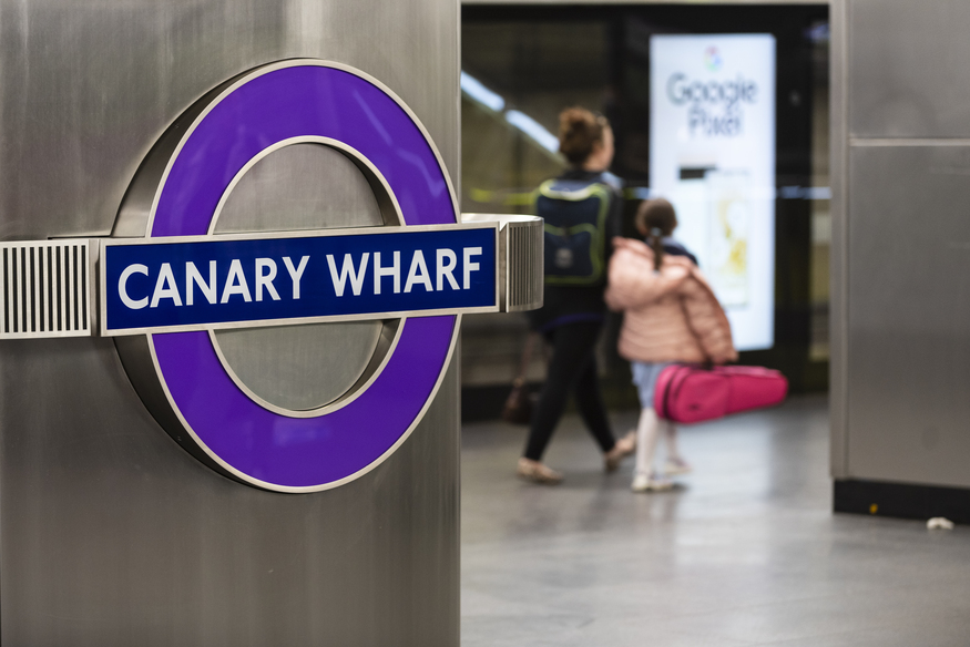 A parent and child walk past a purple Canary Wharf roundel