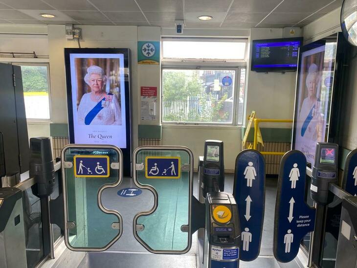 Gates of a train station with a billboard tribute to the Queen