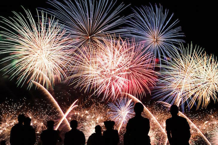 Seven people silhouetted, looking up at fireworks in the sky