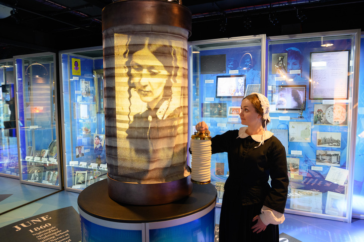 A woman dressed as Florence Nightingale holds a lamp next to an image of Florence herself