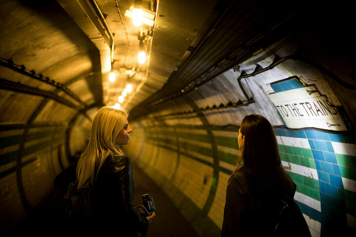 Two women explore the tunnel of an abandoned tube station