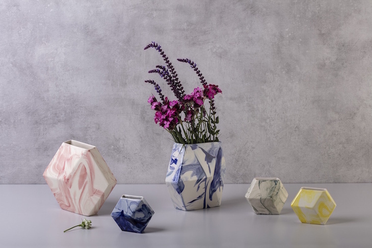 Five marble-effect hexagonal vases of varying sizes and colours on a table. The largest, in the centre, contains some sprigs of lavender