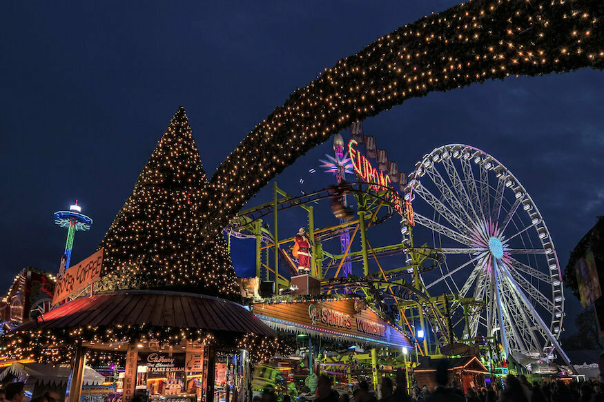 A Christmas tree and arch covered in fairy lights at Hyde Park Winter Wonderland, with the observation wheel and other rides visible in the background