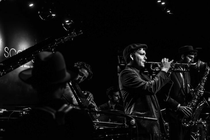 A black and white photograph of musician Pete Horsfall playing the trumpet while performing live on stage