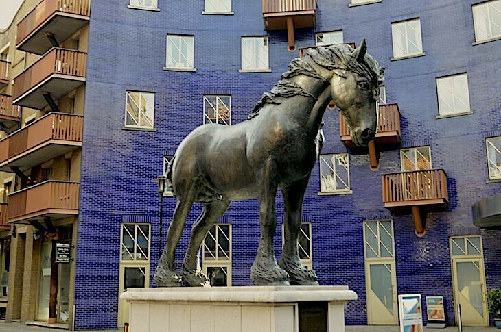 A large black sculpture of a horse with a blue-tiled building behind