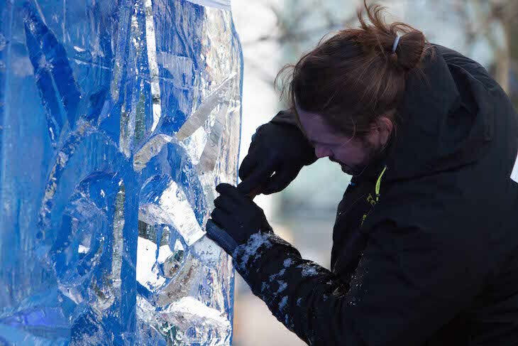 Dressed in thick coat and gloves, an ice sculptor using a tool works on carving a sculpture out of ice 