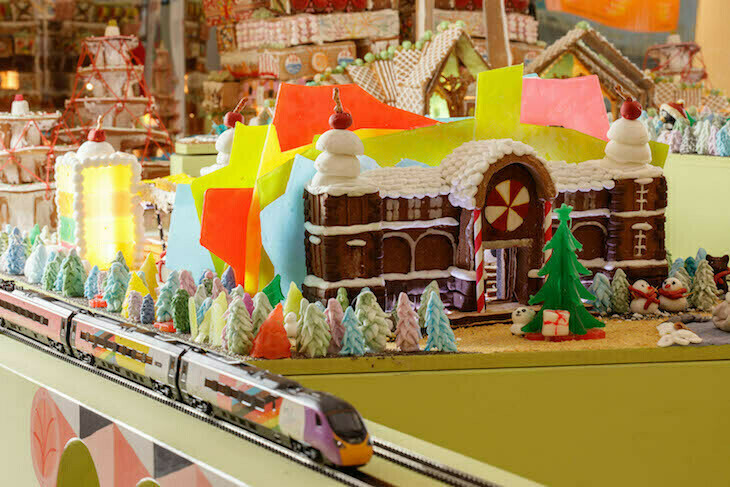 A train station and other buildings made from gingerbread, with a model train going past