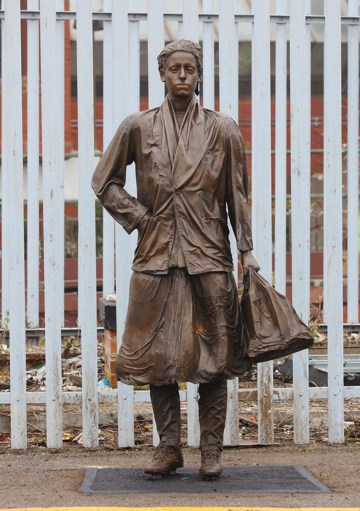 Bronze statue of a woman on a platform holding a bag