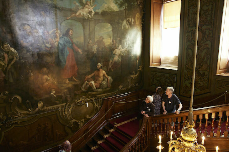 Two conservators look up at a huge painting on a staircase