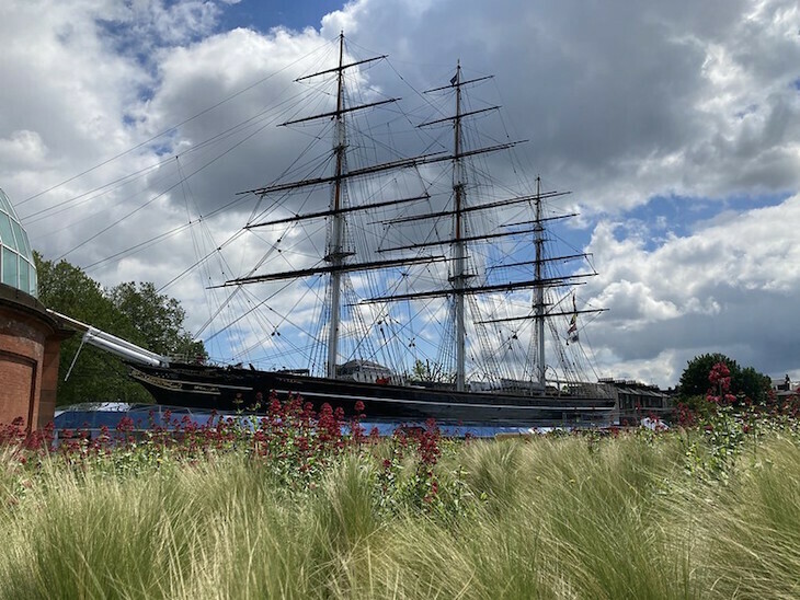 The sails of the Cutty Sark, behind a bed of flowers and grass