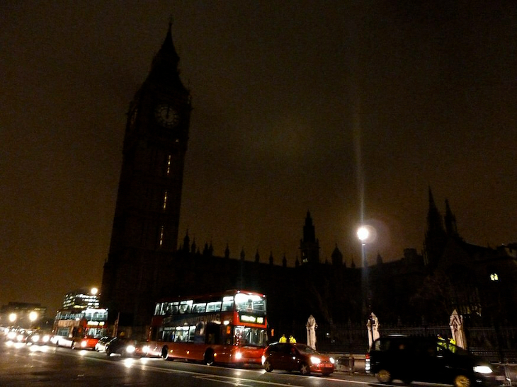 The Houses of Parliament and Elizabeth Tower in complete darkness. Vehicles passing by on the road outside still have their lights on. 