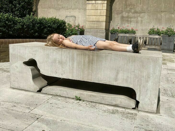 A young girl sits on a bench which has a cutaway of a sausage dog in the side