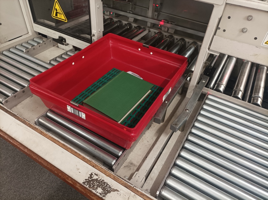 A green book in a red tray ready to go on a conveyor belt
