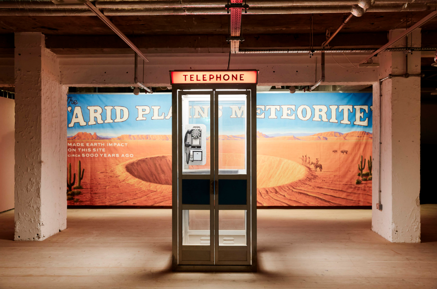 Things to do this week in London: a old-fashioned public telephone, with a backdrop of a poster about a meteorite in the desert - part of the Wes Anderson exhibition