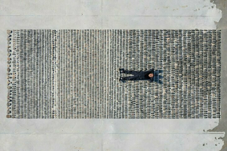 Artist Ai Weiwei lying down on a pattern of pebbles on the ground