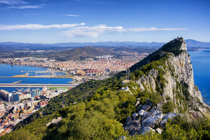 A mountain peak, with a harbour and town visible behind it.